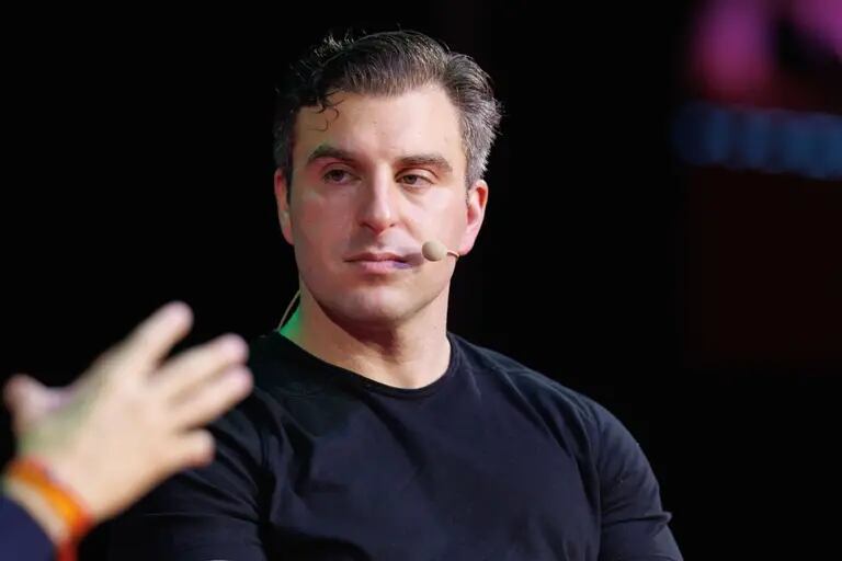 Brian Chesky, CEO do Airbnb usando uma blusa preta e prestando atenção em um interlocutor durante palestradfd
