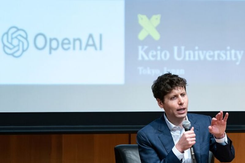 Foto de Sam Altman em primeiro plano. Atrás, um telão com o logotipo da OpenAI e da Keio University